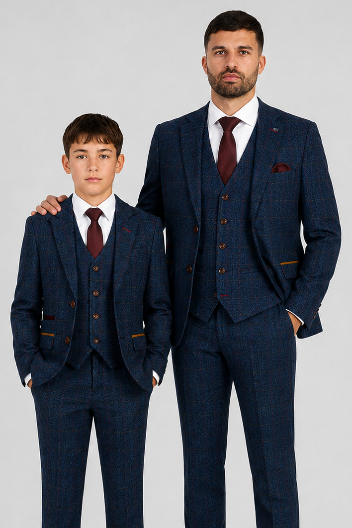 An adult man and a young boy wearing matching navy blue three-piece suits with a subtle micro-check pattern, white dress shirts, burgundy ties, and brown leather shoes, standing against a light grey studio background.