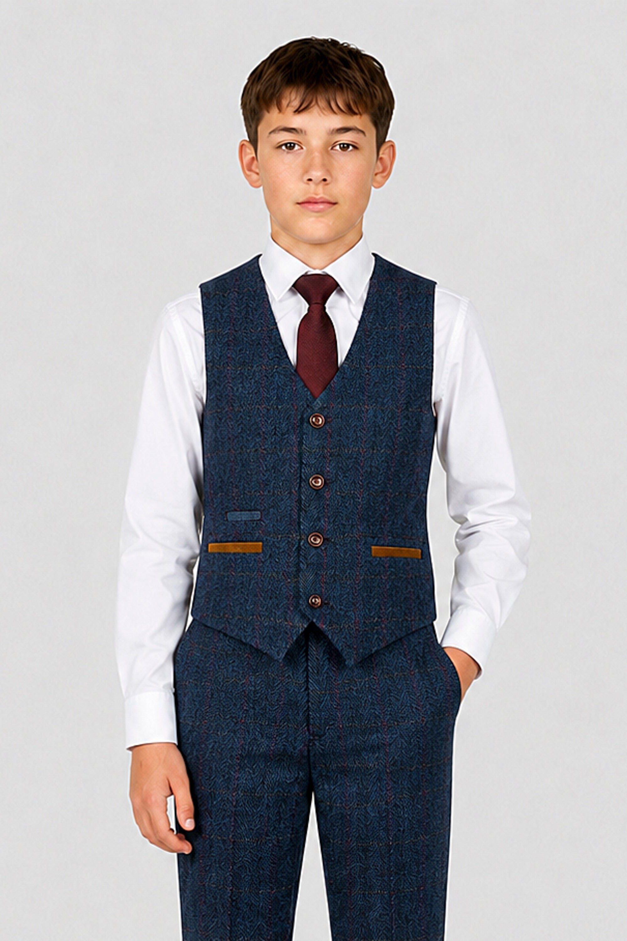 A young boy modeling a navy blue tweed three-piece suit with a white dress shirt, a dark red tie, and brown pocket accents, shot against a light gray studio background.